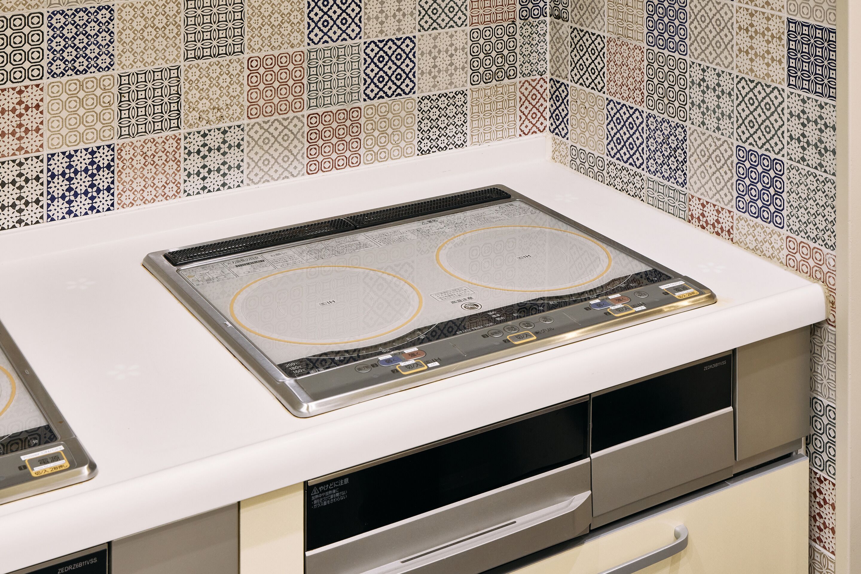 A kitchen with a built-in stove and oven, a white countertop, and patterned backsplash tiles.