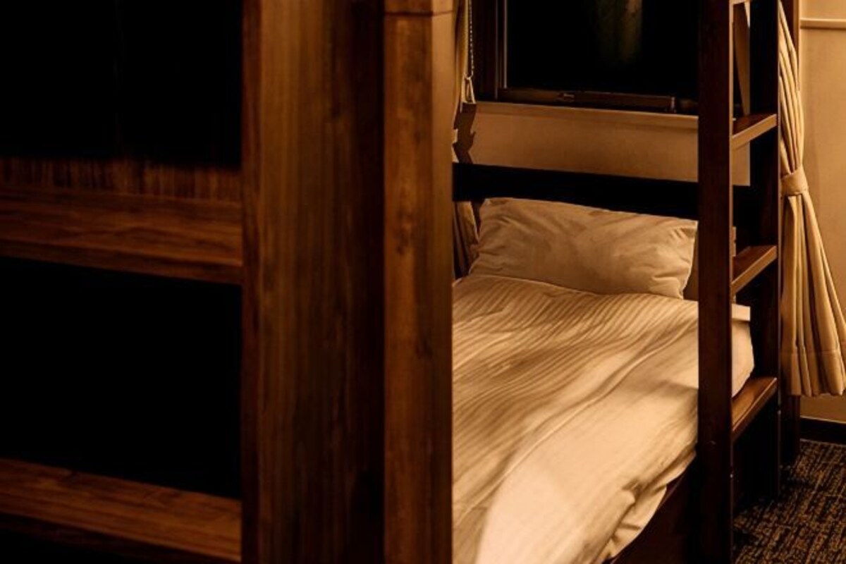 Un lit superposé avec une structure en bois, une fenêtre au-dessus et un rideau sur le côté droit.