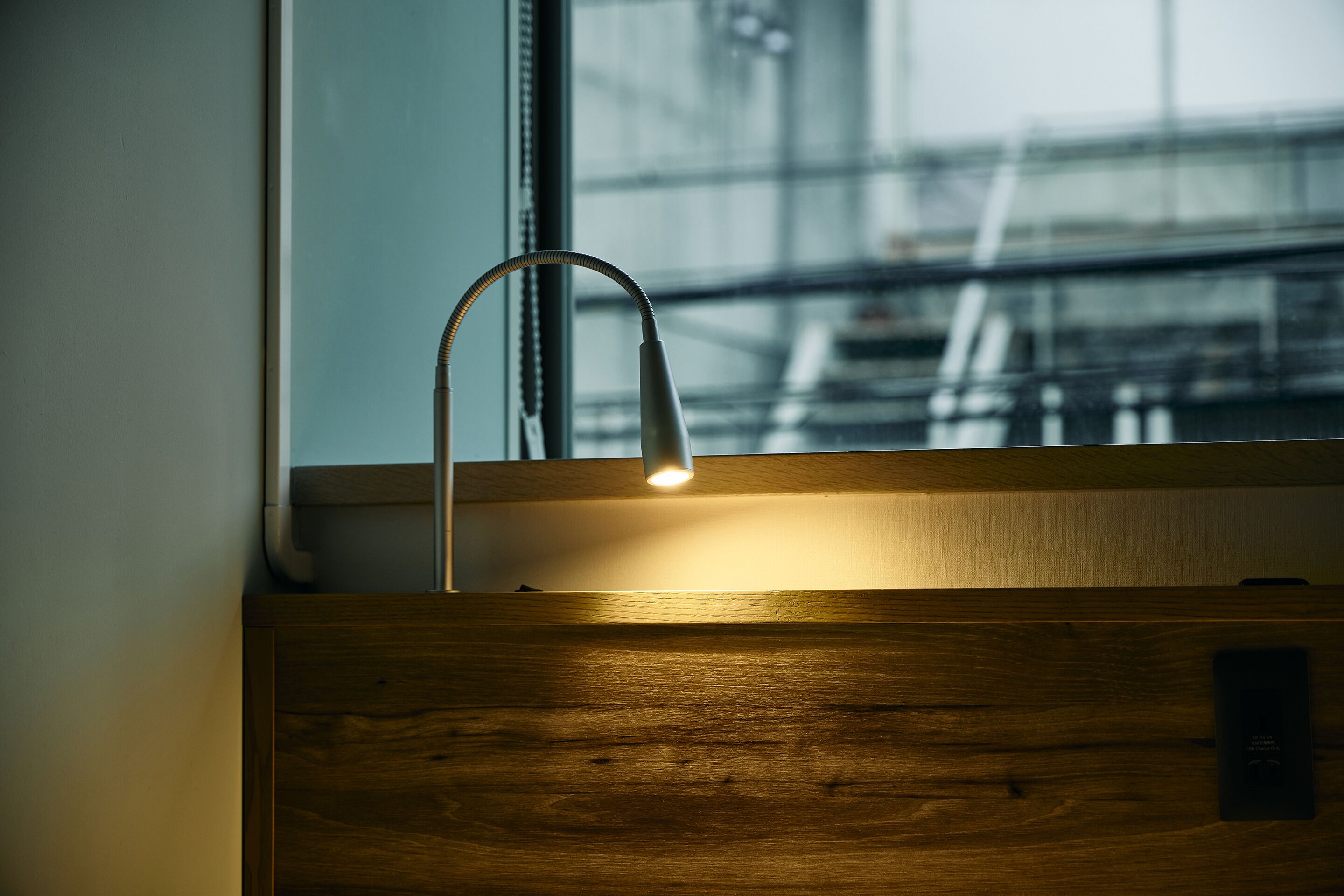 A wooden cabinet with a modern faucet and a window with a view of an industrial structure.