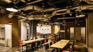 A spacious dining area with multiple tables and chairs, a brick wall, and industrial ceiling features. - Kyoto Guesthouse HIVE - Hostel (Kyoto)