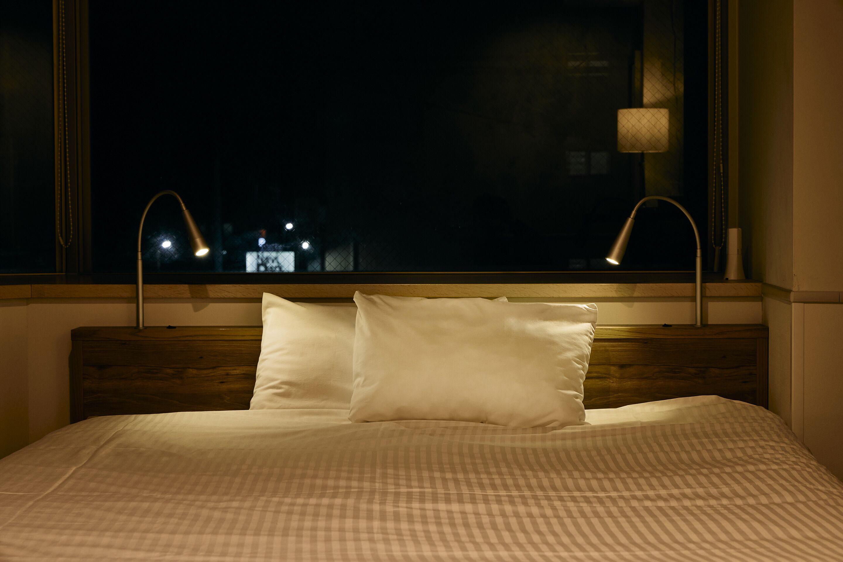 A neatly made bed with a checkered bedspread and two pillows, positioned in front of a window with two bedside lamps.