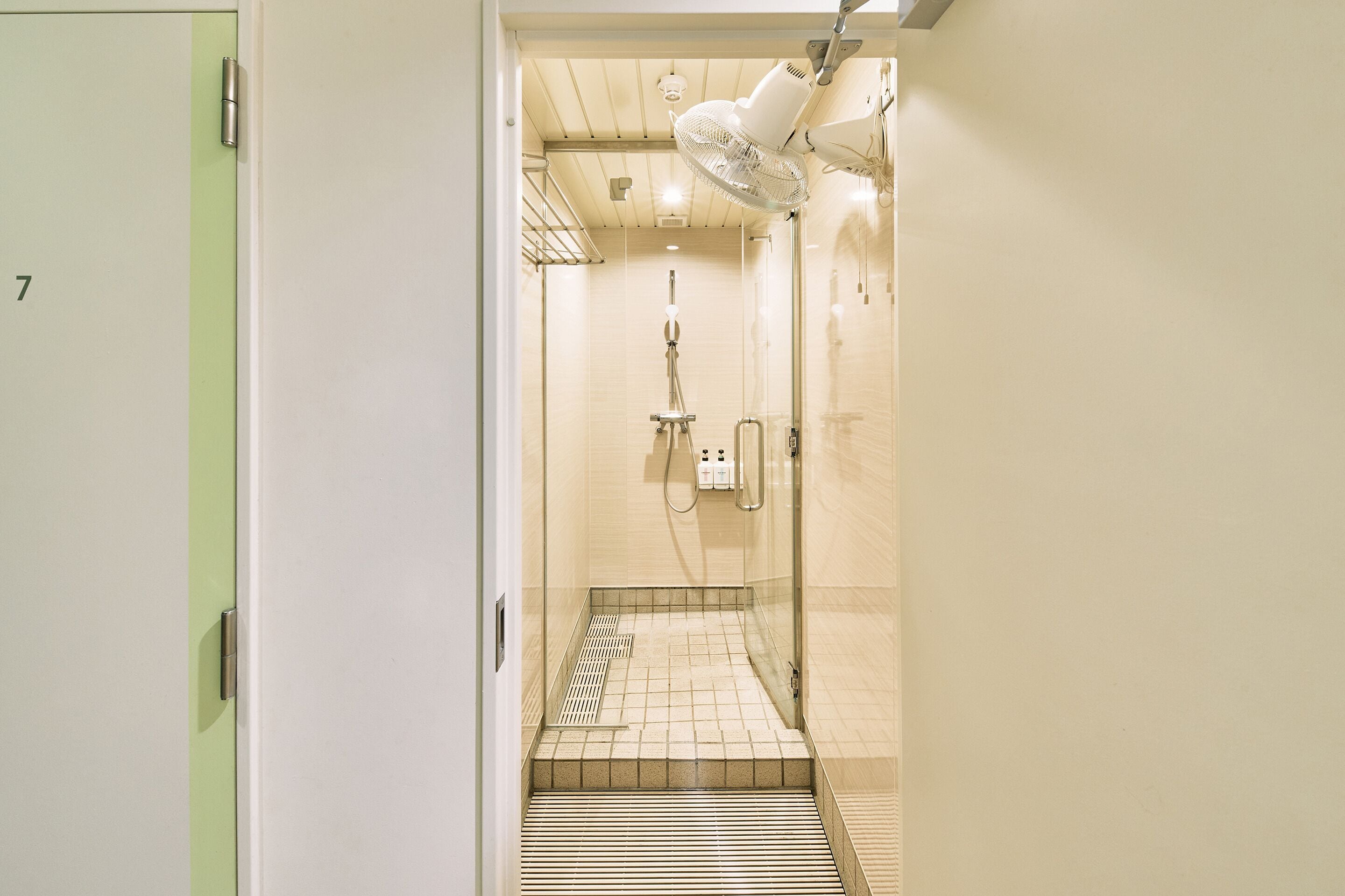 Une salle de bain moderne dotée d’une douche à paroi de verre, d’une sortie d’eau visible et d’un ventilateur fixé au plafond.