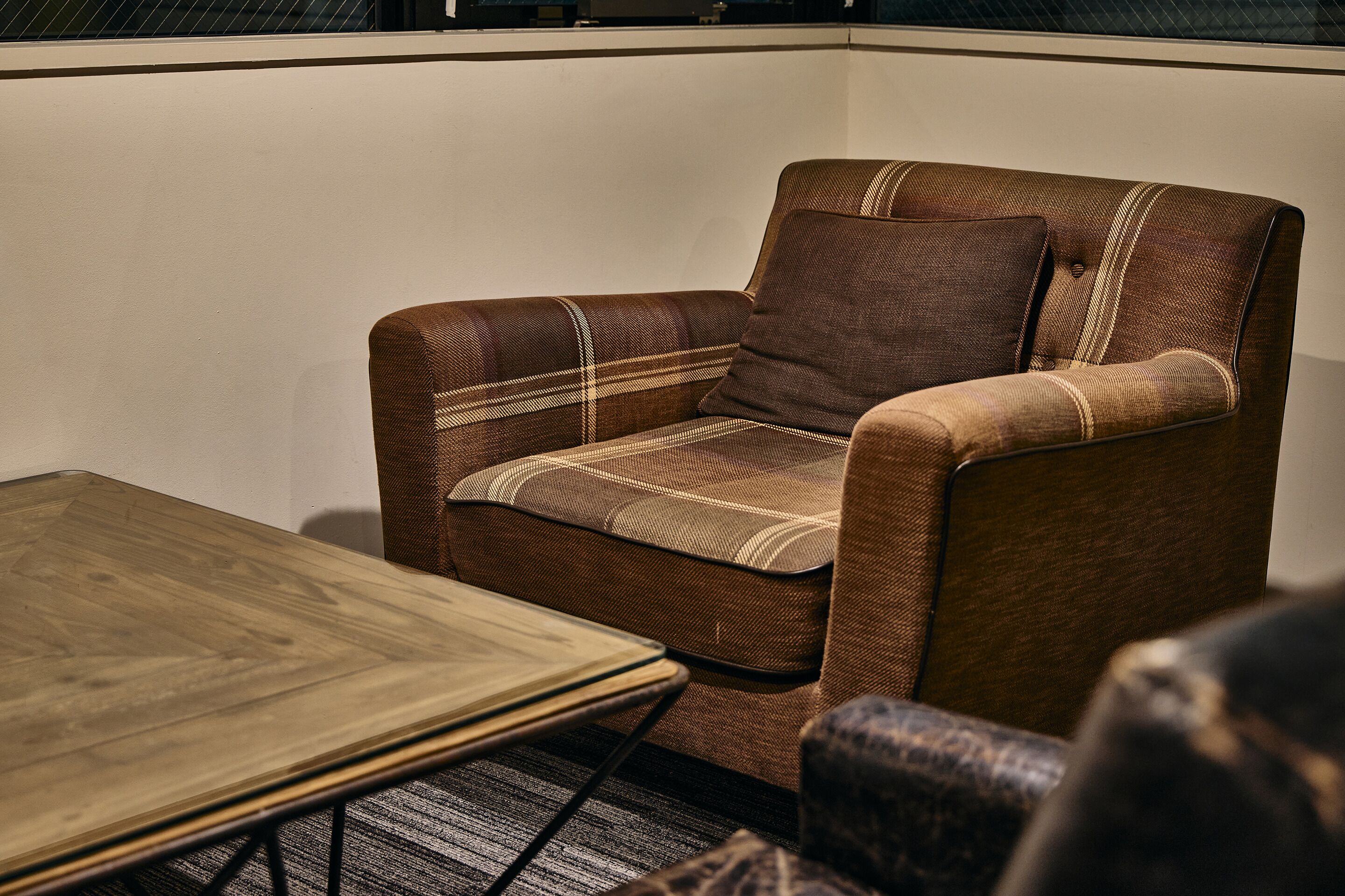 Un sillón marrón con estampado de cuadros, una mesa de centro de madera y una alfombra estampada.