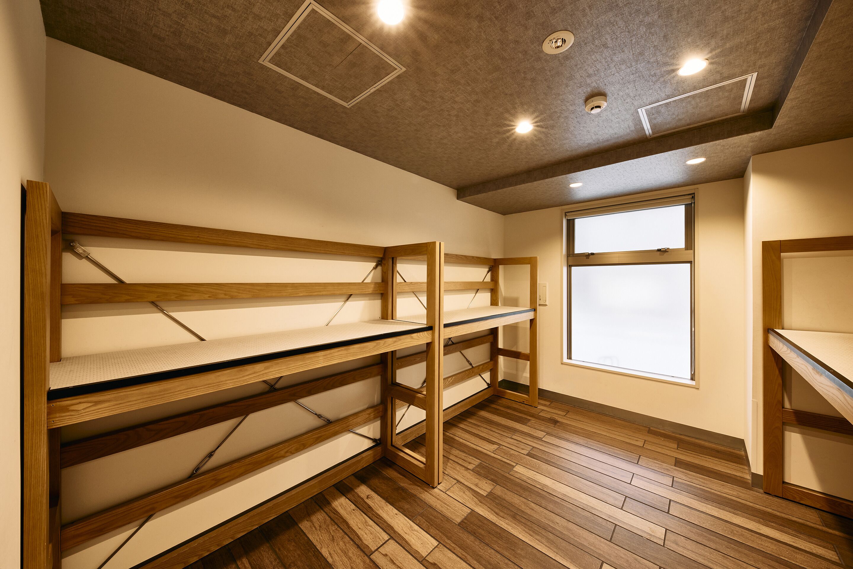 A room with wooden bunk beds, a large window, and a ceiling with recessed lighting.