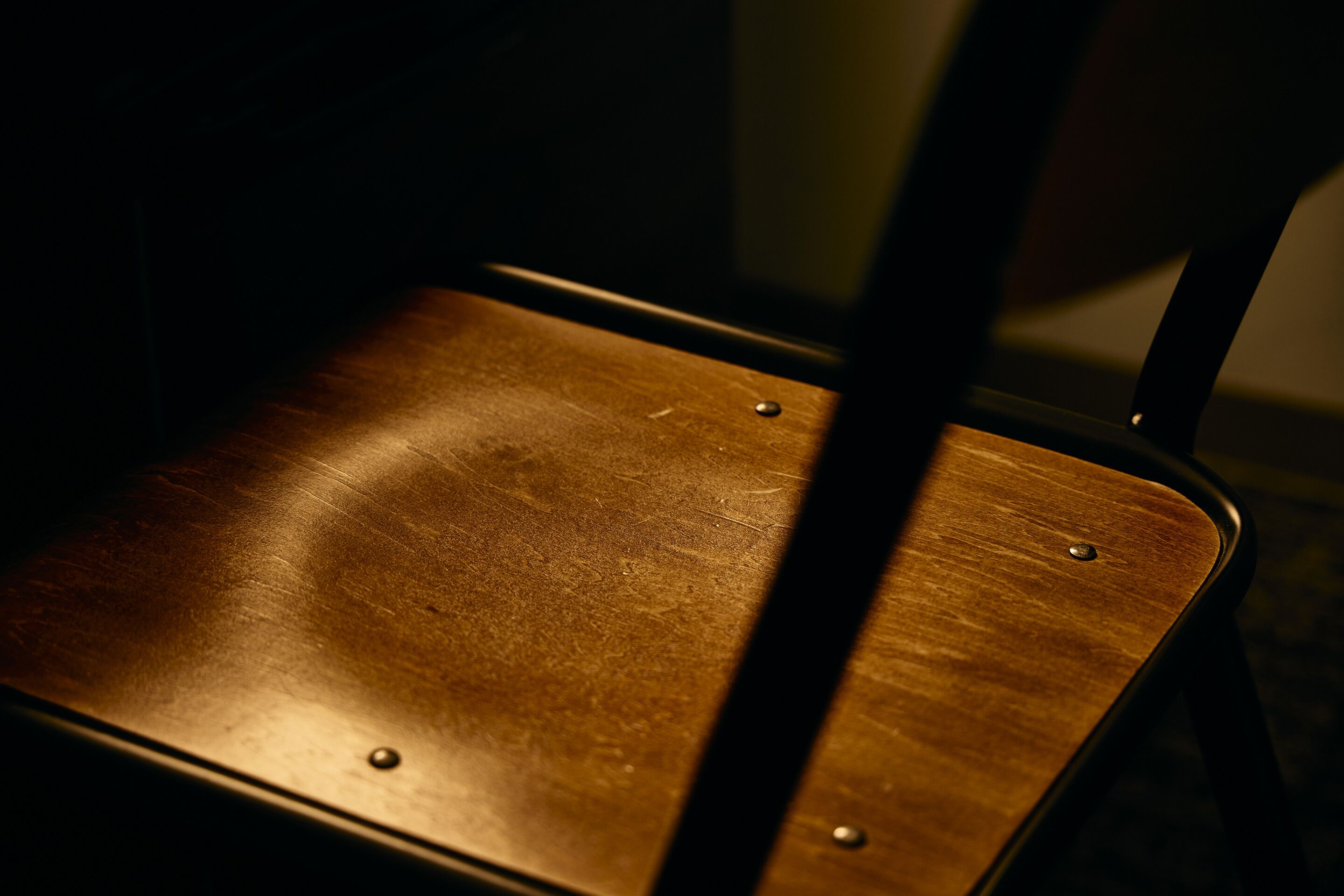 A close-up of a wooden chair with metal legs and rivets.
