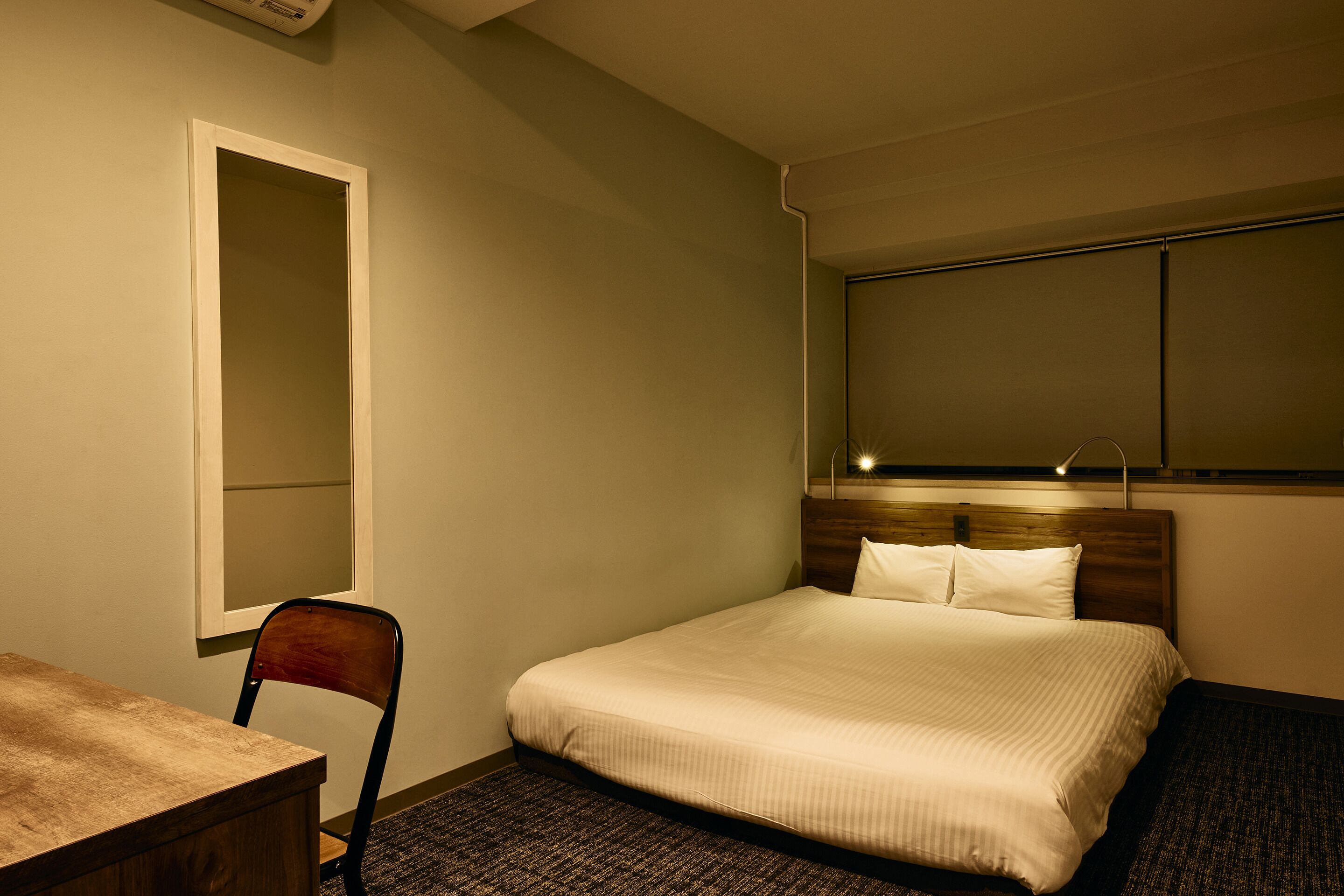 A hotel room with a single bed, a wooden desk, a chair, and a large mirror on the wall.