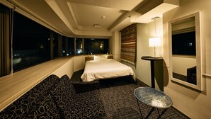 Une chambre d’hôtel avec un grand lit, un canapé, une petite table et une fenêtre donnant sur la ville, avec une vue particulièrement belle la nuit.