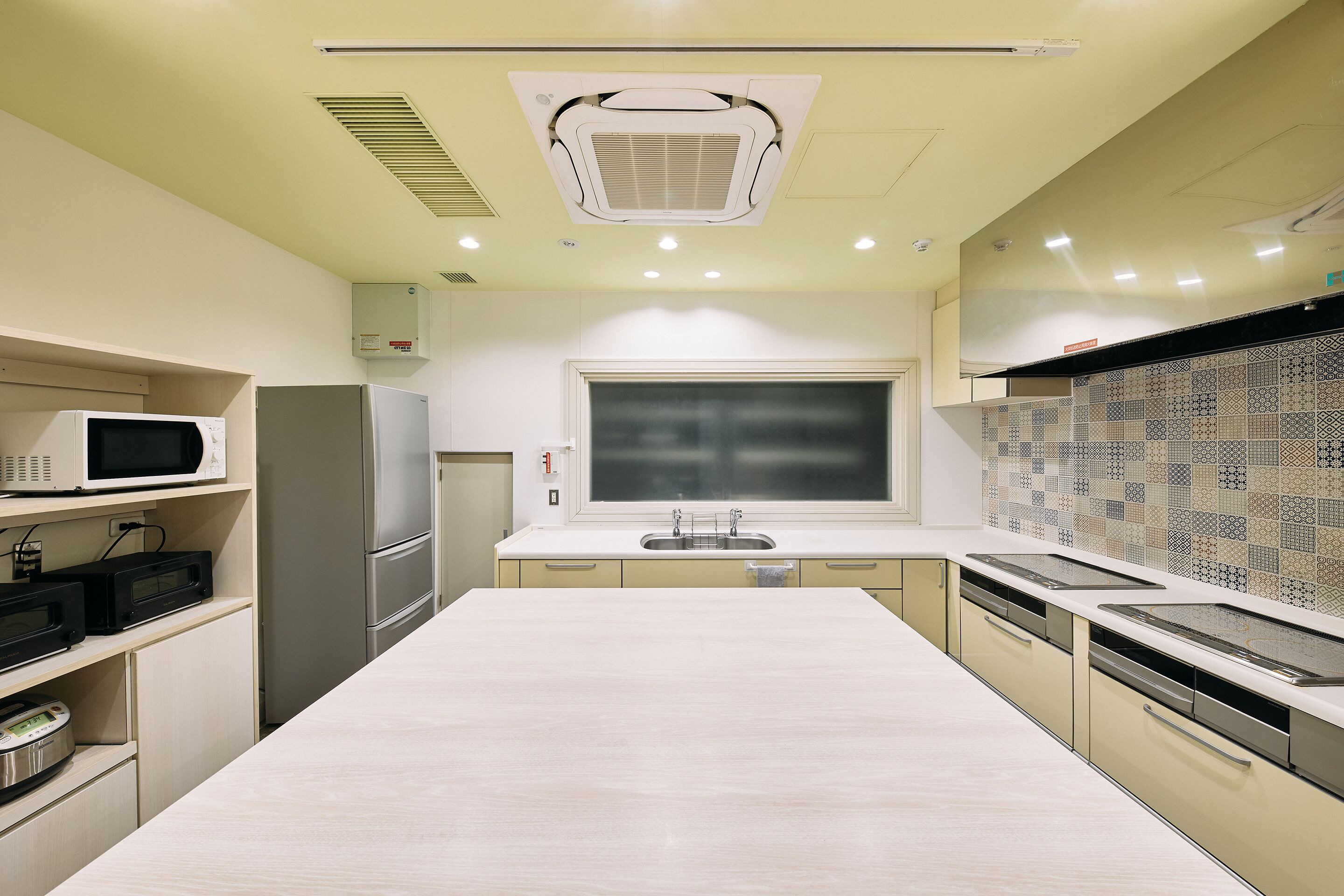 A modern kitchen with a large island, built-in appliances, and a patterned backsplash.