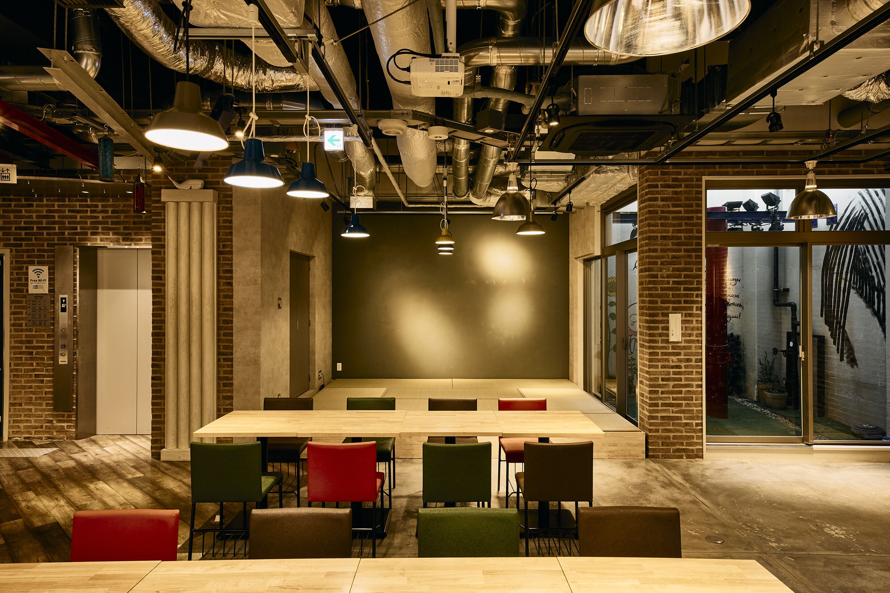 Un salón de conferencias con una larga mesa y múltiples sillas, techo estilo industrial con tuberías expuestas y un amplio ventanal con vistas al exterior.
