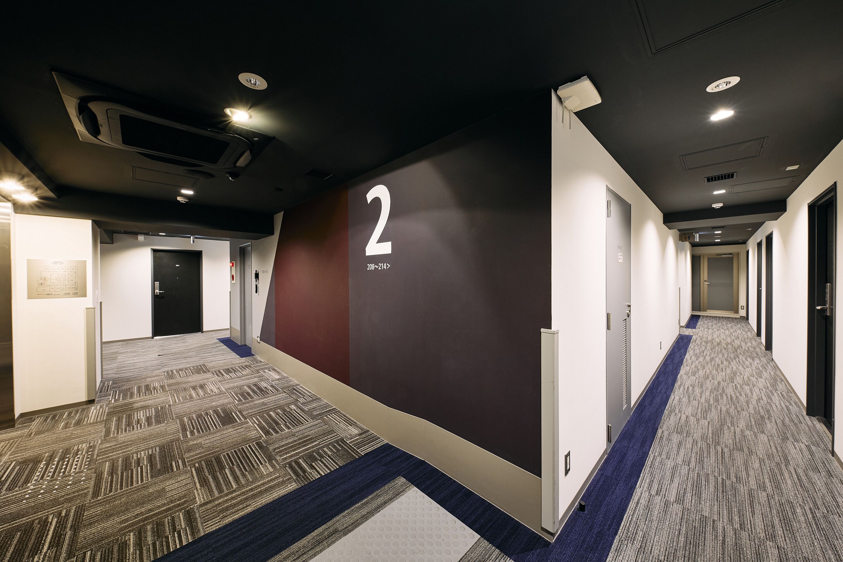 A hallway with carpeted floors, a wall with a number '2' sign, and doors leading to rooms.