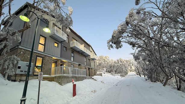 Un edificio de varios pisos con balcones, una calle cubierta de nieve y árboles.