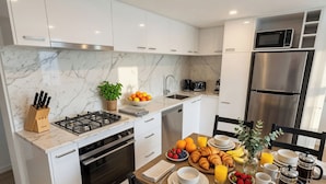 Una cocina moderna con armarios blancos, una estufa a gas, un microondas y un refrigerador de acero inoxidable.