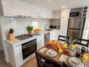 Una cucina moderna con mobili bianchi, piano cottura a gas, forno a microonde e frigorifero in acciaio inossidabile.