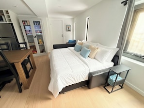 Quarto moderno com cama, mesa de cabeceira e área de escritório.