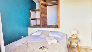 A bedroom with a bed, a nightstand, a lamp, and a wooden shelf above the bed. - Villa of the Three Monkeys. Between the beach and the mountains. (Saint-Pierre)