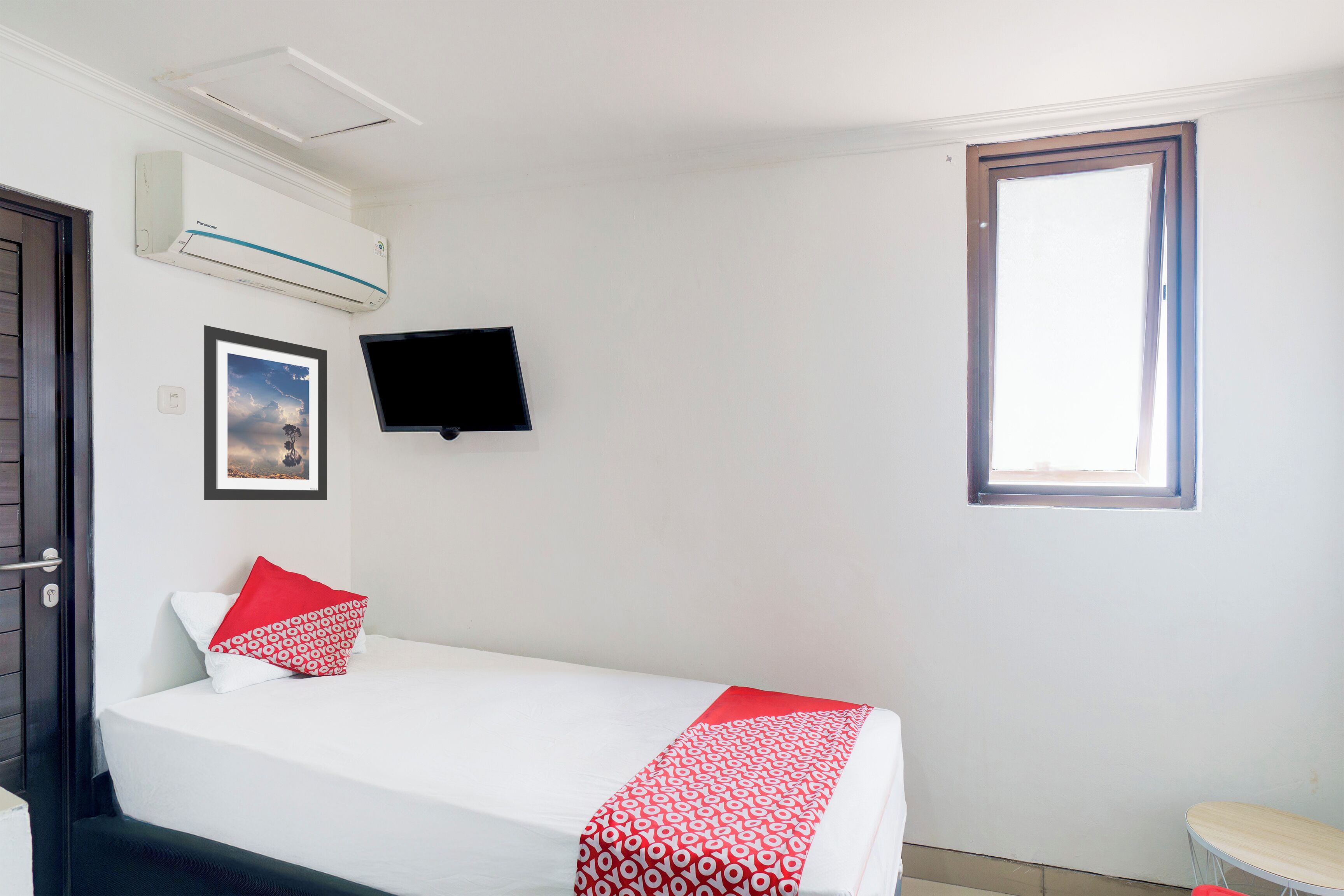 Una habitación de hotel con una cama, un televisor montado en la pared, una ventana y un equipo de aire acondicionado.