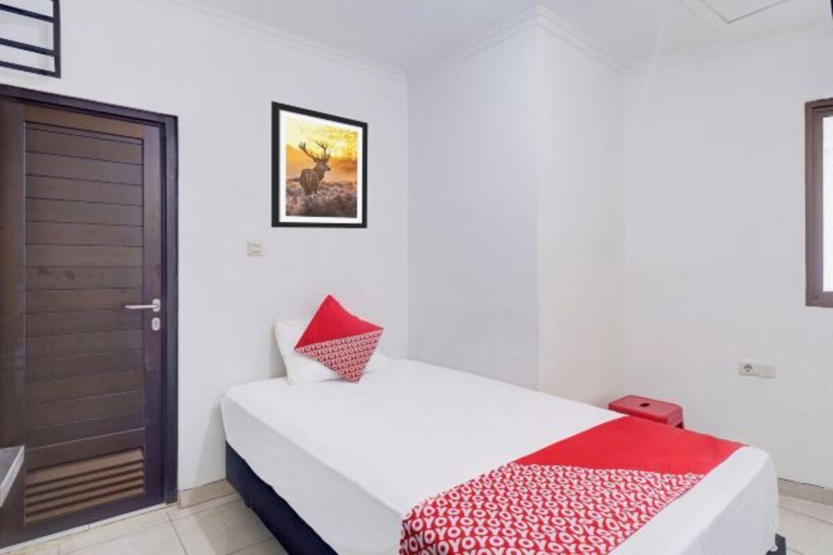 Habitación de hotel con una cama, una puerta, un cuadro en la pared y una almohada roja.