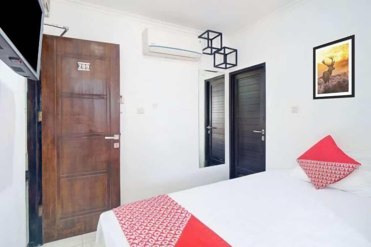A hotel room with a bed, a wooden door, a window, and a wall-mounted air conditioner.
