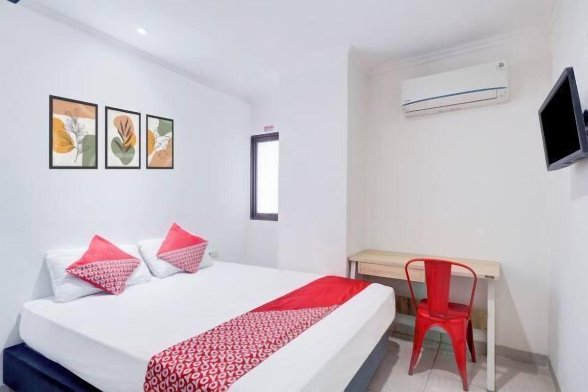 A hotel room with a bed, a desk, a chair, an air conditioner, and wall art.