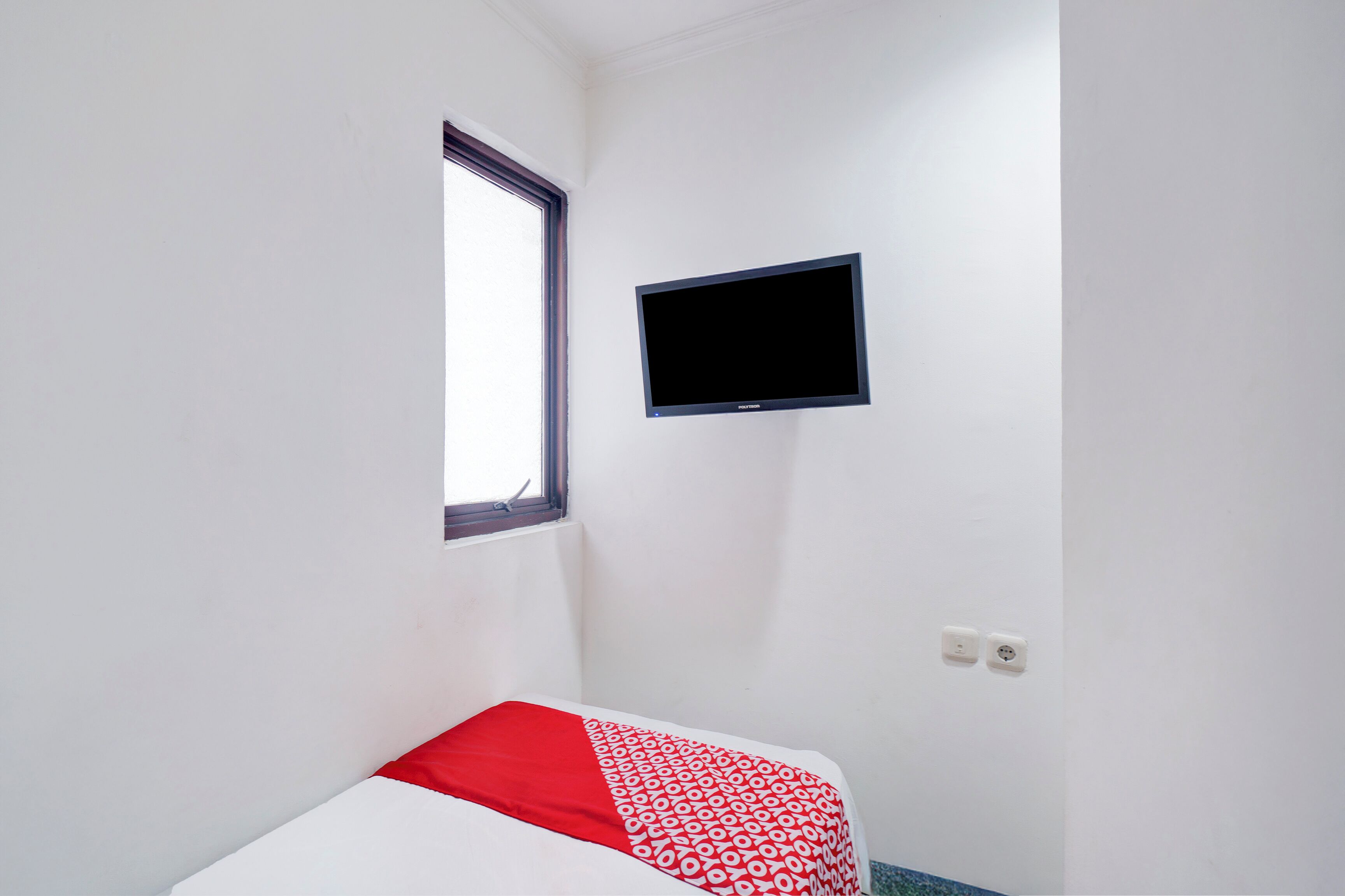 A small, simple room with a bed, a TV mounted on the wall, and a window.