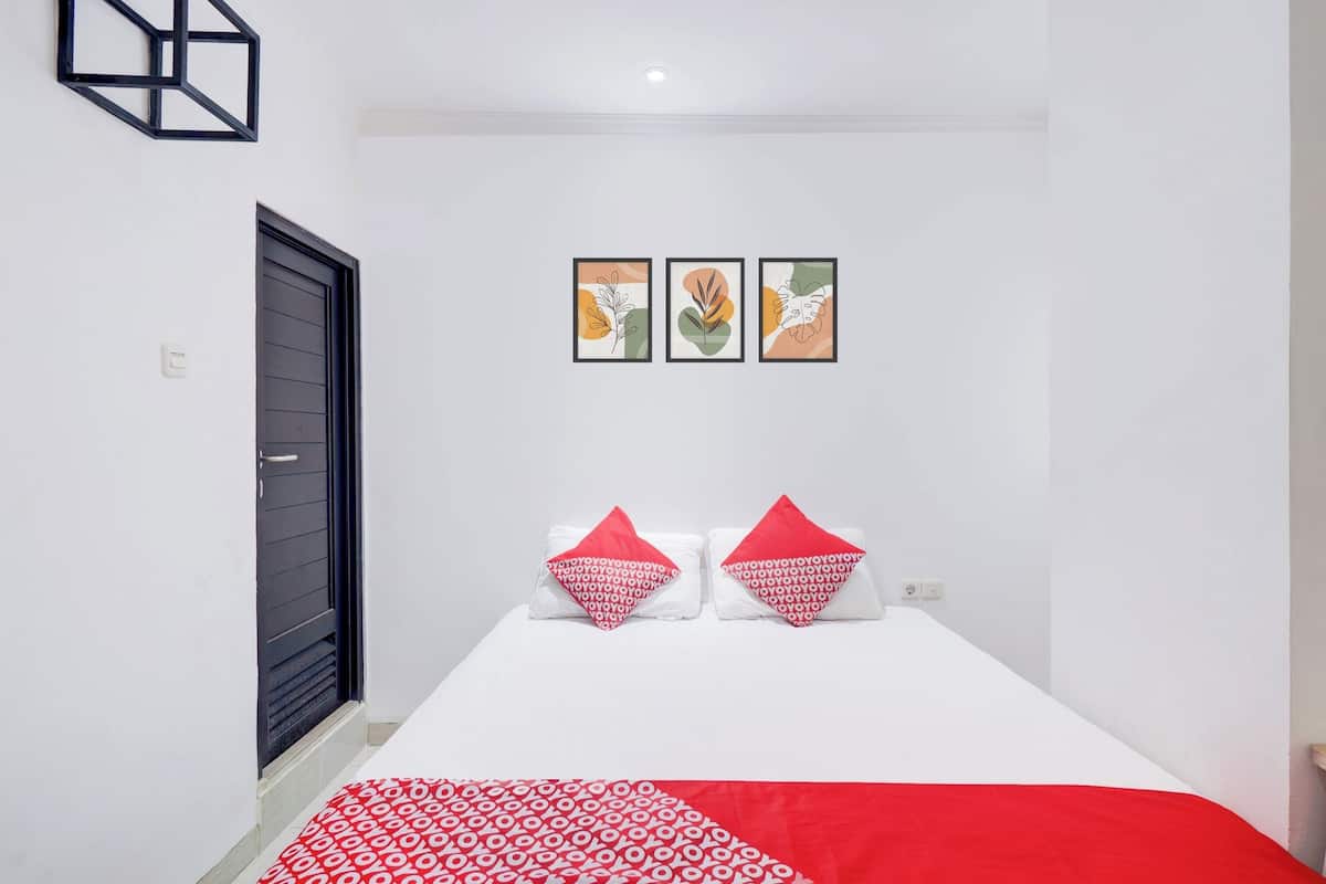 A bedroom with a bed, two pillows, a red and white patterned bedspread, and three framed artworks on the wall.