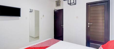 A bedroom with a bed, a TV mounted on the wall, a door, and a mirror.