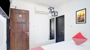Een hotelkamer met een grote houten deur waarop '209' staat, een bed met een wit en rood gebedspread, en een lijst met een foto van een hert aan de muur.