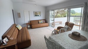 A spacious living area with a brown sofa, a dining table with chairs, and a view through large windows.