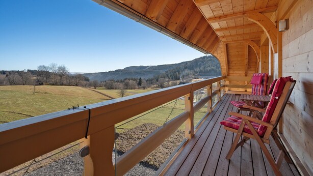 Eine Holzterrasse mit Blick auf ein Wiesfeld und Hügel.
