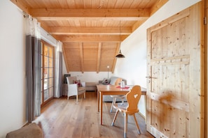 A room with a wooden ceiling, a dining table with chairs, a sofa, and a large wooden door.