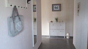 Un couloir avec un porte-manteau, un miroir, une armoire blanche et une petite plante en pot.