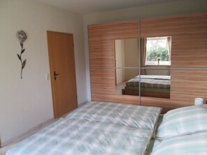 Une chambre à coucher avec un lit, une armoire, un miroir et une fenêtre.