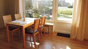 Un coin repas avec une table et des chaises en bois, une fenêtre donnant sur un paysage verdoyant et une porte avec des rideaux.