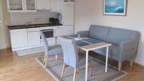 Une cuisine compacte avec des meubles blancs, une machine à café et un coin repas comprenant une table et deux chaises.