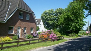 Une maison à deux étages, construite en briques, avec un toit en pente, un porche à l’avant et une clôture en bois.