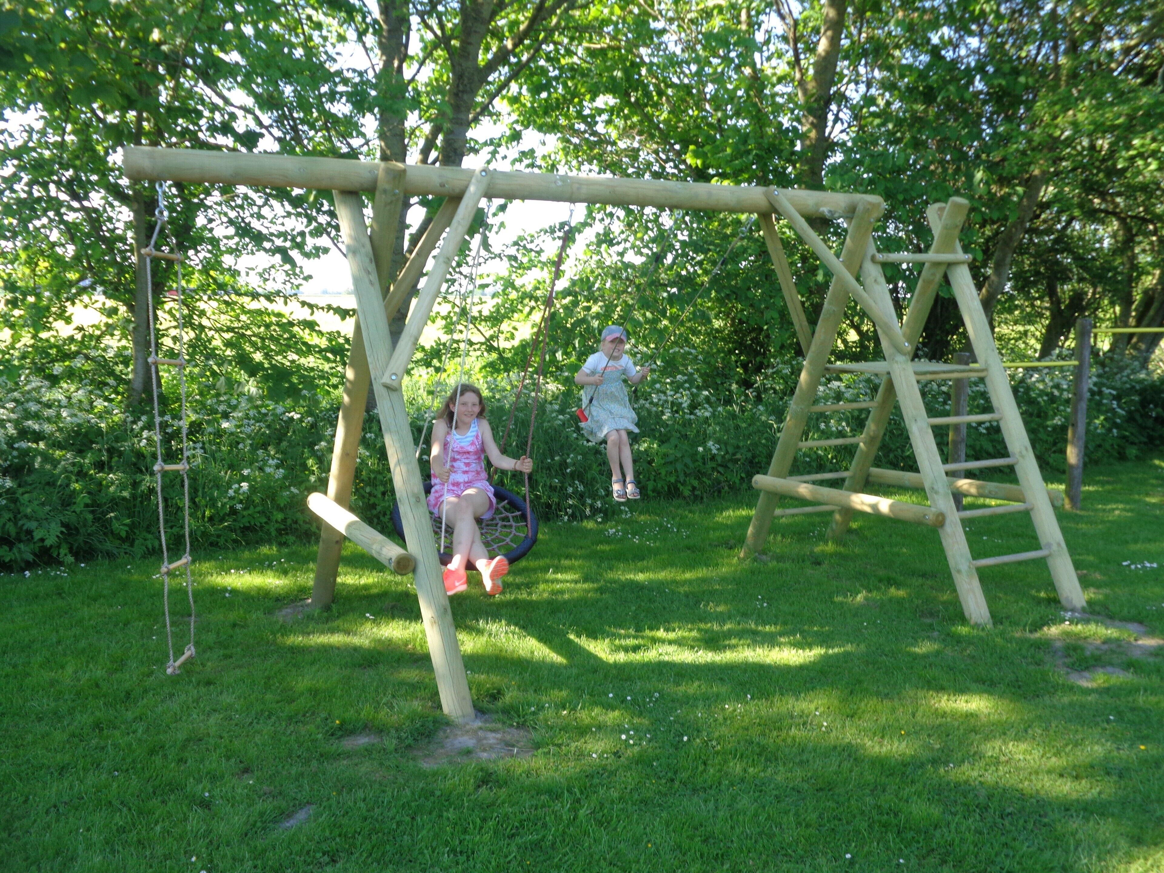 Un ensemble de balançoires en bois installé dans un espace herbeux, avec des arbres en arrière-plan.