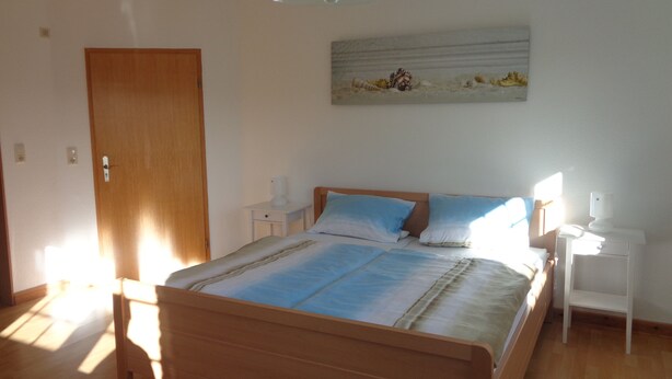 Un dormitorio con una cama de madera, mesitas de noche, una obra de arte colgada en la pared y una puerta.