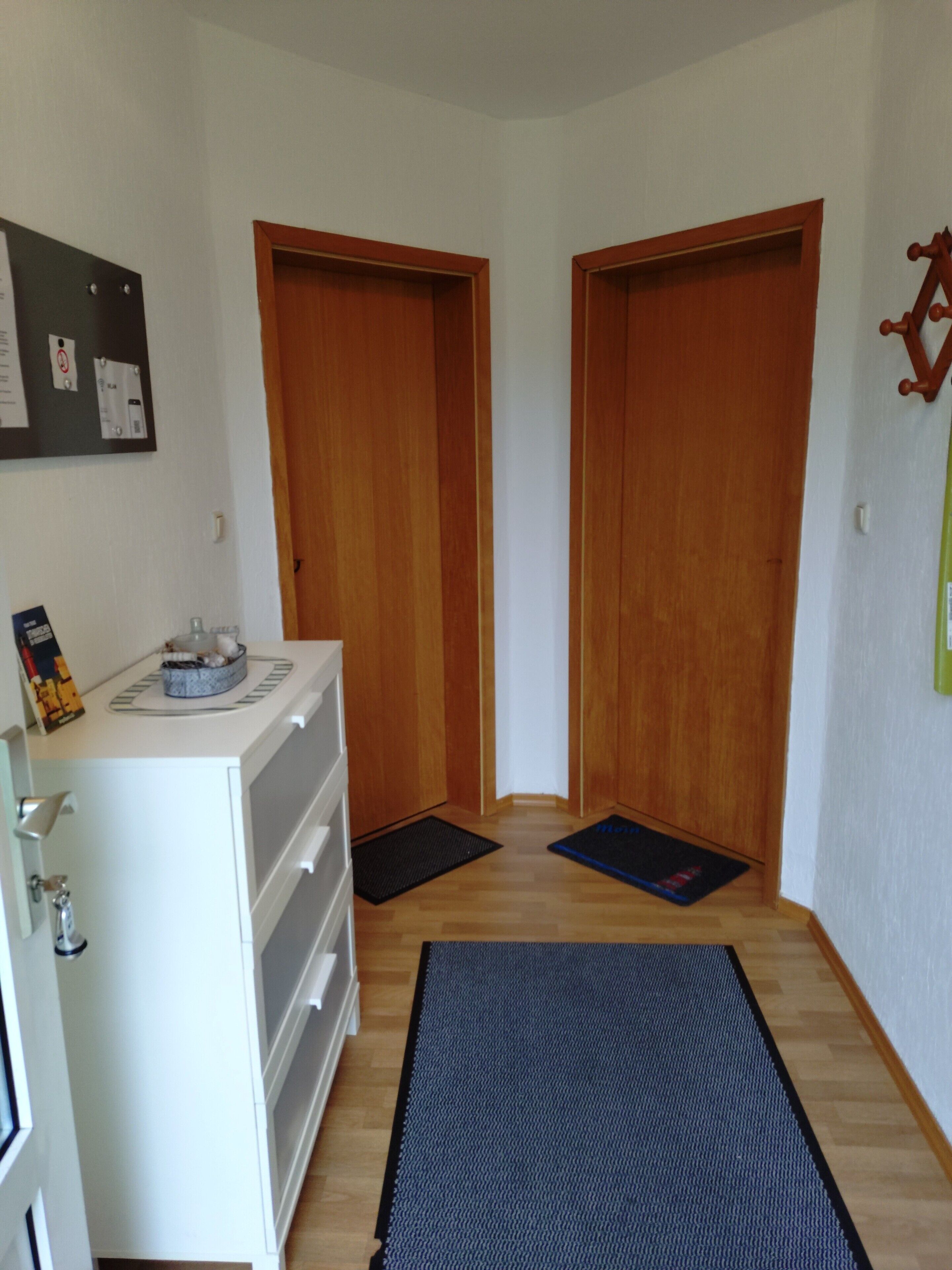 Ein Flur mit Holztüren, einem weißen Schrank und einer schwarzen Matte auf dem Boden.