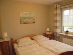 Une chambre avec deux lits, un tableau au mur, une fenêtre avec des rideaux et une table de chevet avec une lampe.