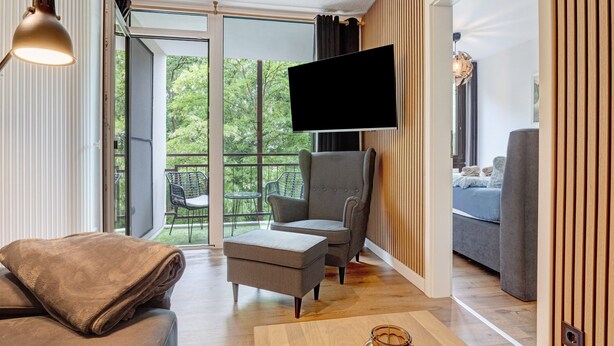 A modern living room with a sofa, armchair, ottoman, and a flat-screen TV mounted on the wall.