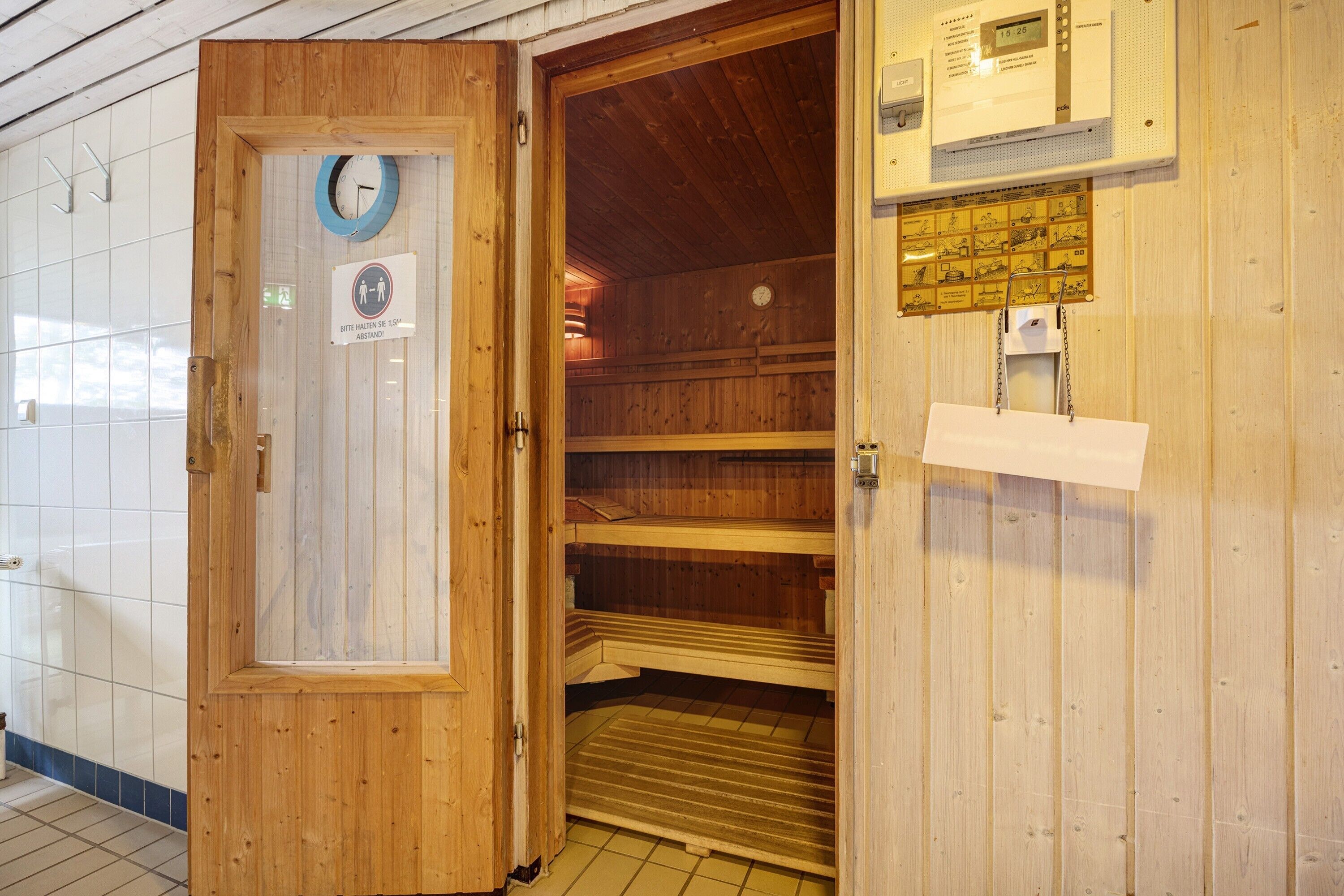 Un sauna avec des murs en bois, une porte, une horloge et un panneau de commande.
