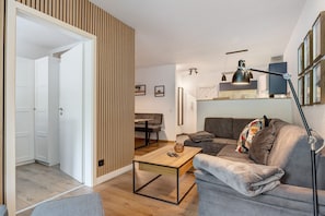 Un salon moderne avec un canapé, une table basse et une lampe. On aperçoit à l’arrière-plan un coin repas avec une table et des chaises.