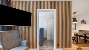 A modern living room with a sofa, a dining table, and a TV mounted on the wall.