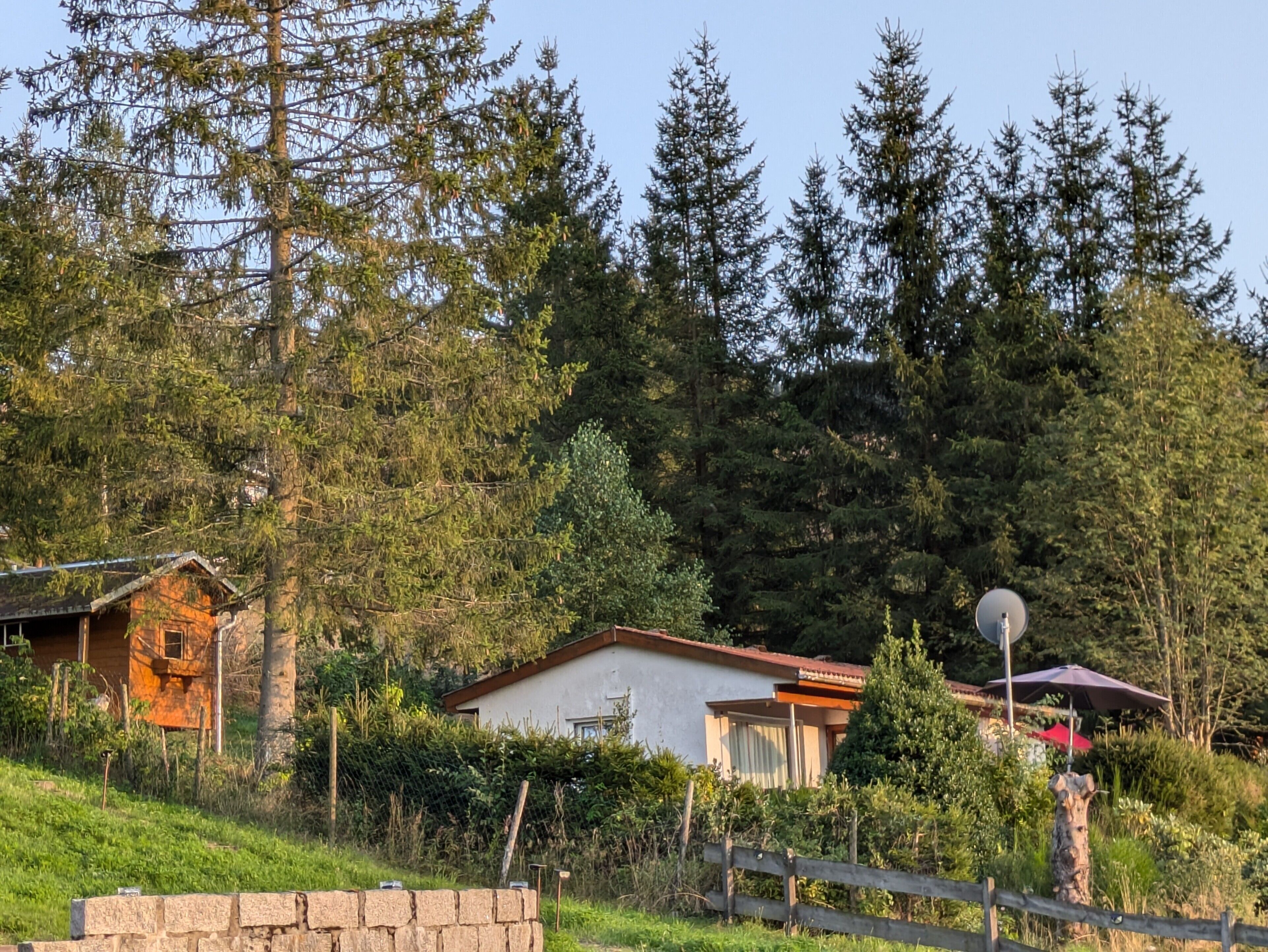 A rural house with a stone wall, a wooden fence, and a satellite dish.