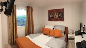 Un dormitorio con cama, una mesita de noche, una lámpara, un control remoto y un cuadro en la pared.