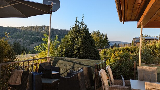 Un patio exterior con mobiliario de mimbre, una antena parabólica y vistas a una ladera boscosa.