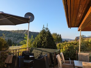 Een terras buiten met rieten meubilair, een schotelantenne en uitzicht op een bebost helling.