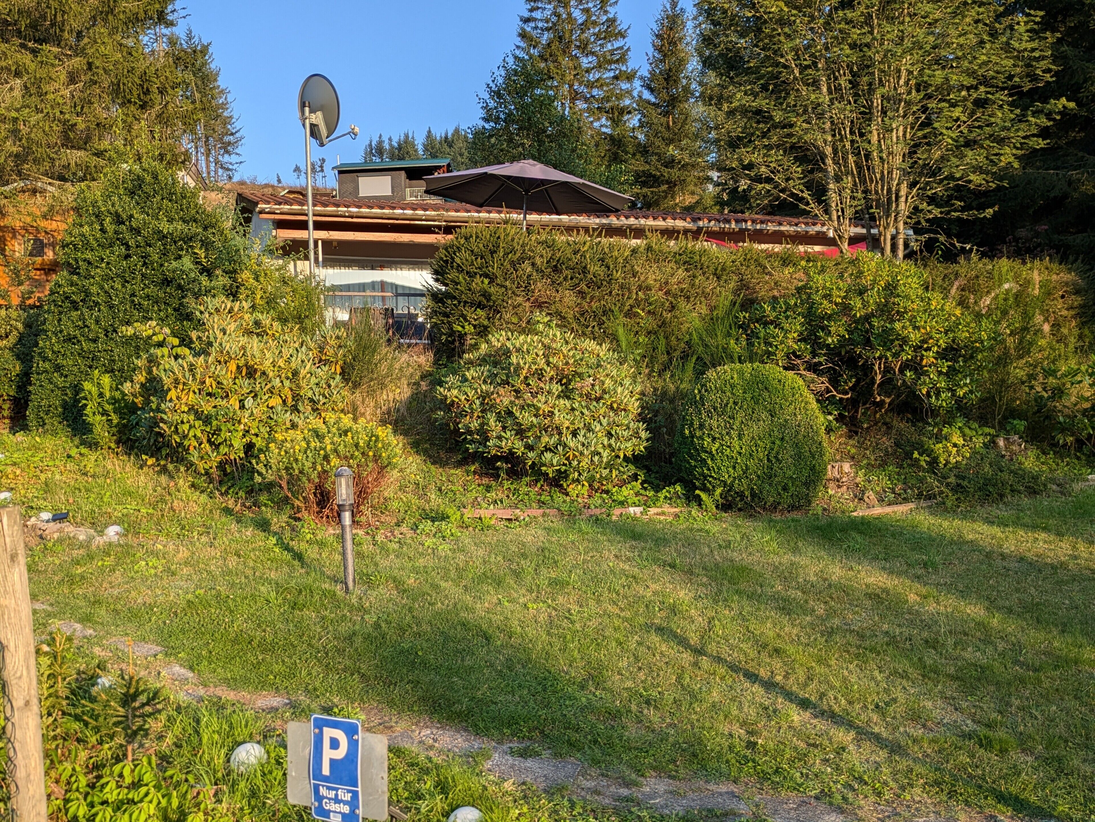 Ein Haus, umgeben von üppiger Vegetation, einer Satellitenschüssel und einem Parkschild.