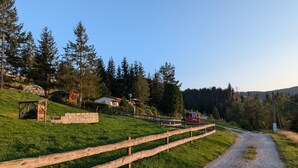 Paisaje rural con un camino de grava, valla de madera y un vehículo rojo.
