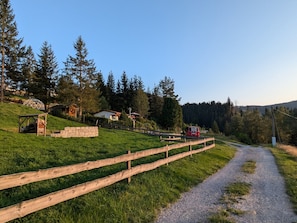 Ländliche Landschaft mit einem Schotterweg, Holzzaun und einem roten Fahrzeug.